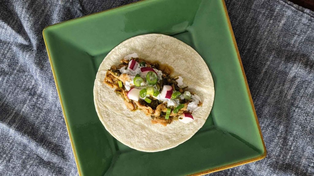 Photo of a tortilla filled with vegan chile verde on a green plate