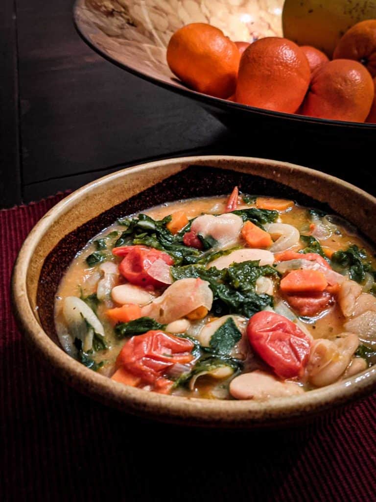 photo of a bowl of butter beans and mustard greens on a table next to a bowl of mandarins