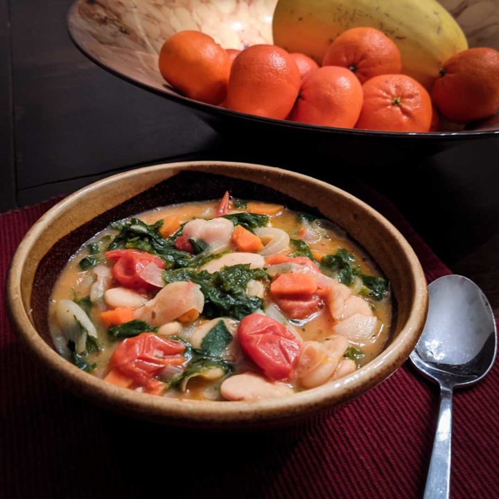 Photo of a bowl of butter beans and mustard greens on a red placemat with a bowl of fruit and vegetables in the background.