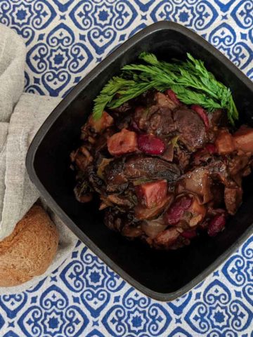 Photo of a bowl of mushroom stew on a blue and white tablecloth with a roll