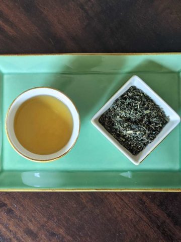 Overhead photo of a cup of nettle tea next to a small dish filled with the dry herbal blend.