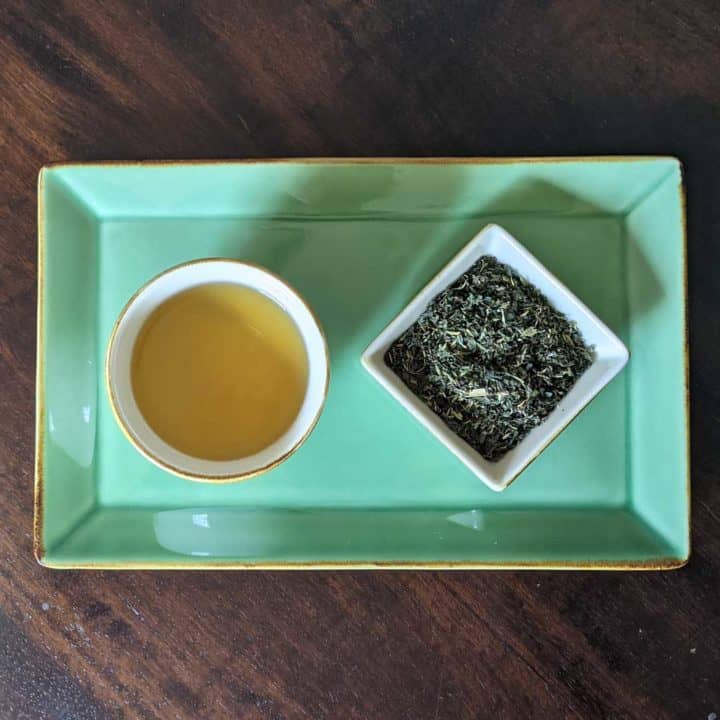 Overhead photo of a cup of nettle tea next to a small dish filled with the dry herbal blend.