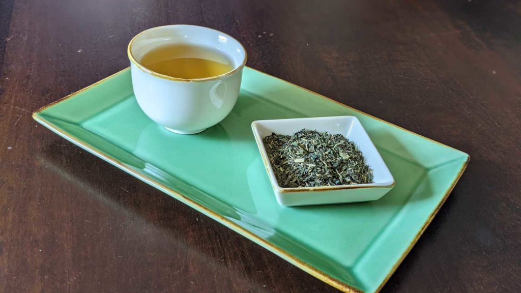 Photo of a cup of nettle tea next to a small dish filled with the dry herbal blend.