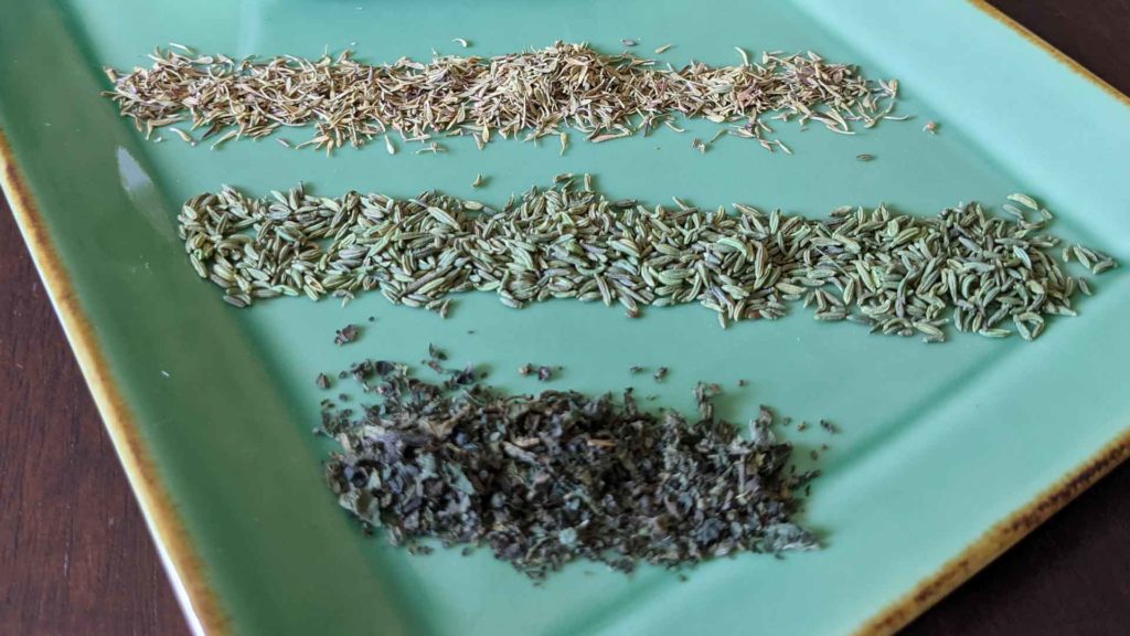 Photo of dried thyme leaves, fennel seeds, and nettle leaves on a green plate.