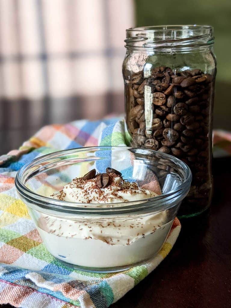 Photo of a small bowl of homemade soy yogurt on a colorful napkin next to a jar of coffee beans