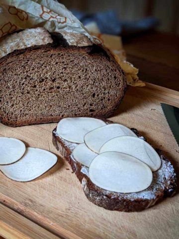 Photo of a loaf of homemade multigrain bread next to a slice of bread with butter and radishes