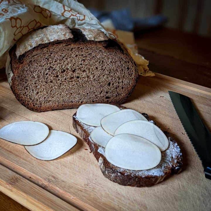 Photo of a loaf of homemade multigrain bread next to a slice of bread with butter and radishes