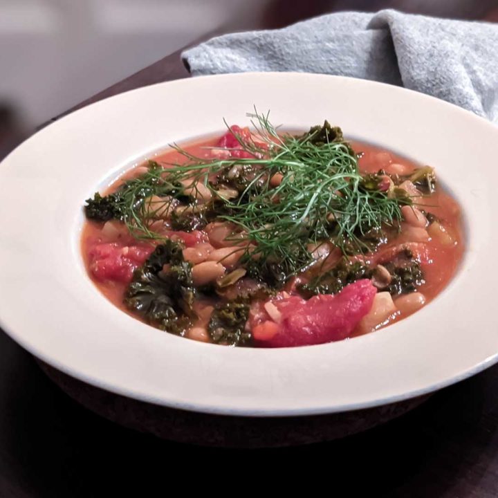 Photo of a bowl of tuscan bean soup on a wooden table, with a cloth napkin