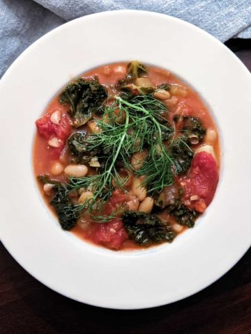 Overhead photo of a bowl of tuscan bean soup with kale and tomatoes