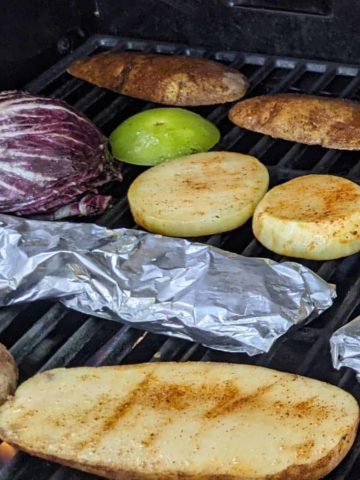 Photo of a grille with slices of potatoes, green tomatoes, radicchio, kohlrabi, and foil packets of sliced beets