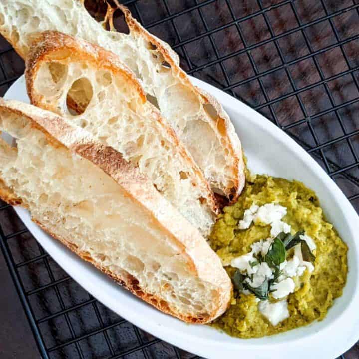 Overhead photo of a dish with fava bean puree and sliced ciabatta bread