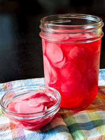 Close up photo of a jar of pickled radishes near a small bowl of them