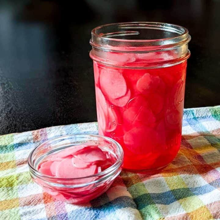 Close up photo of a jar of pickled radishes near a small bowl of them