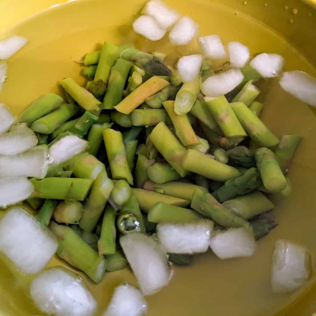 Overhead photo of chopped, blanched asparagus in a bowl of ice water