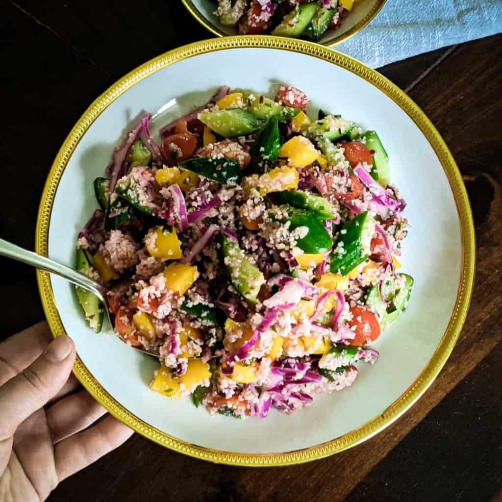 Overhead photo of a hand holding a bowl of cucumber salad with bulgur and mint