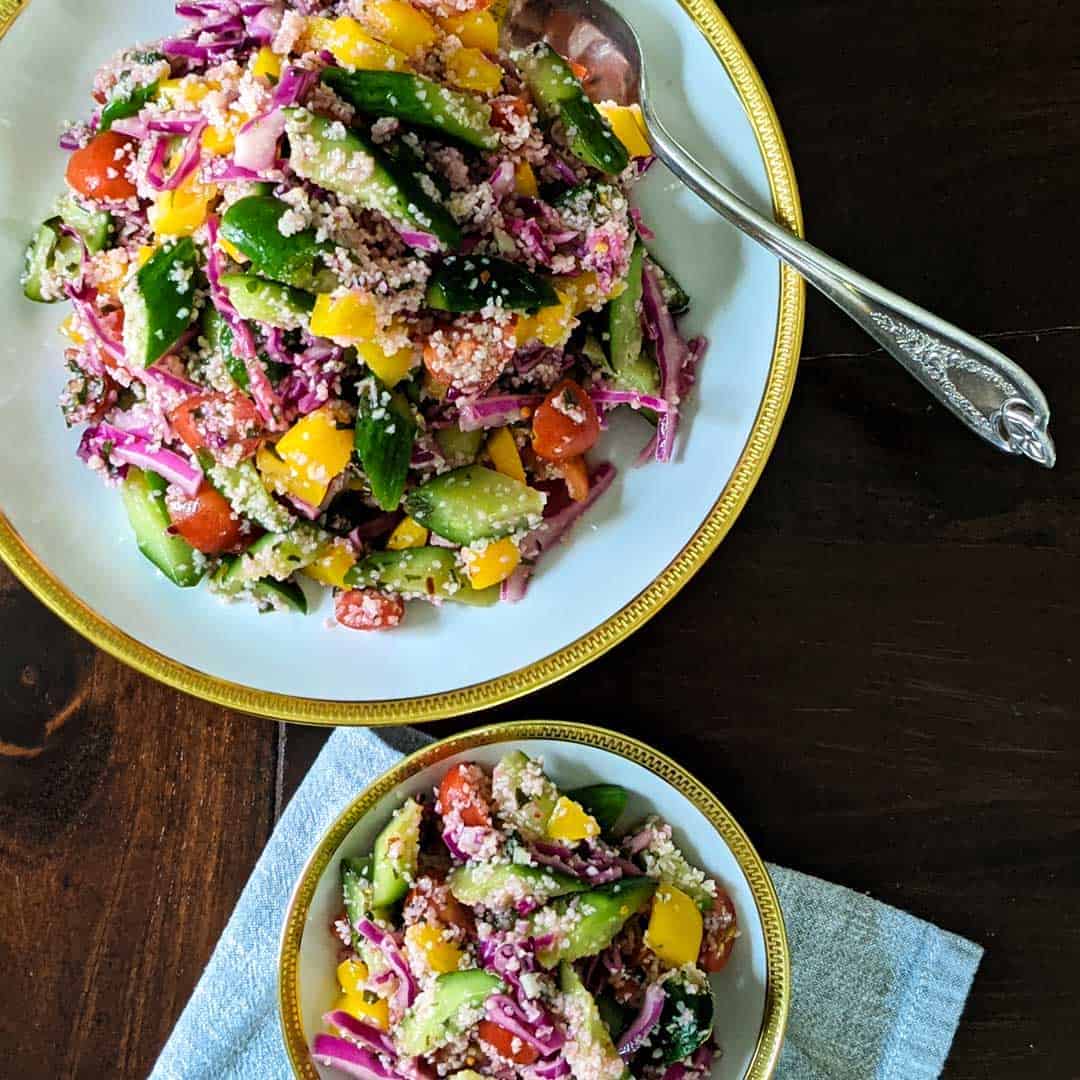 Overhead photo of a large serving bowl of cucumber salad with bulgur and mint next to a smaller bowl holding an individual sized portion