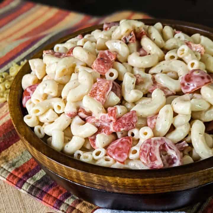 Close up photo of a large wooden bowl full of macaroni salad on a colorful place mat