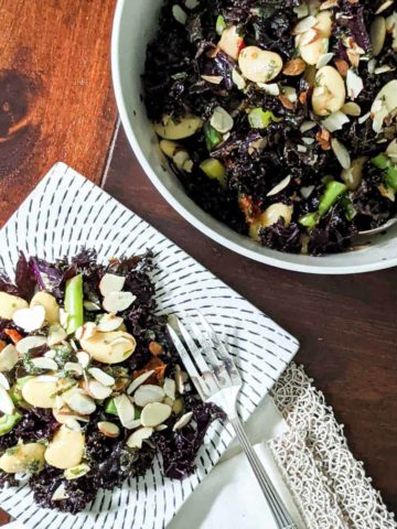 Overhead photo of large bowl of red kale salad next to a single portion on a square plate with a fork and fancy napkin.