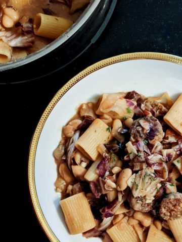 Overhead photo of a pan full of vegan sausage, radicchio, and white bean pasta next to a full bowl on a stovetop.