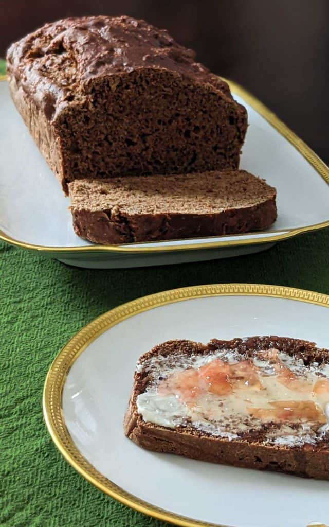 Photo of a sliced loaf of vegan apple ginger quick bread. One slice is on a plate with vegan butter and rose jam.