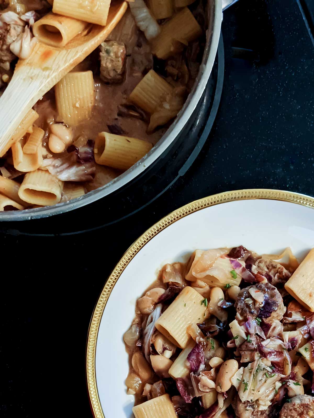 Overhead photo of a pan and bowl of pasta with vegan sausage, radicchio, and white bean pasta