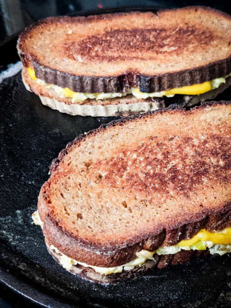 Photo of a cast iron pan with two vegan broccoli grilled cheese sandwiches