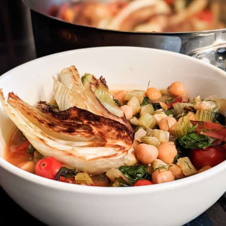 Photo of a bowl of fennel, swiss chard, and chickpea stew next to a full pan on the stovetop