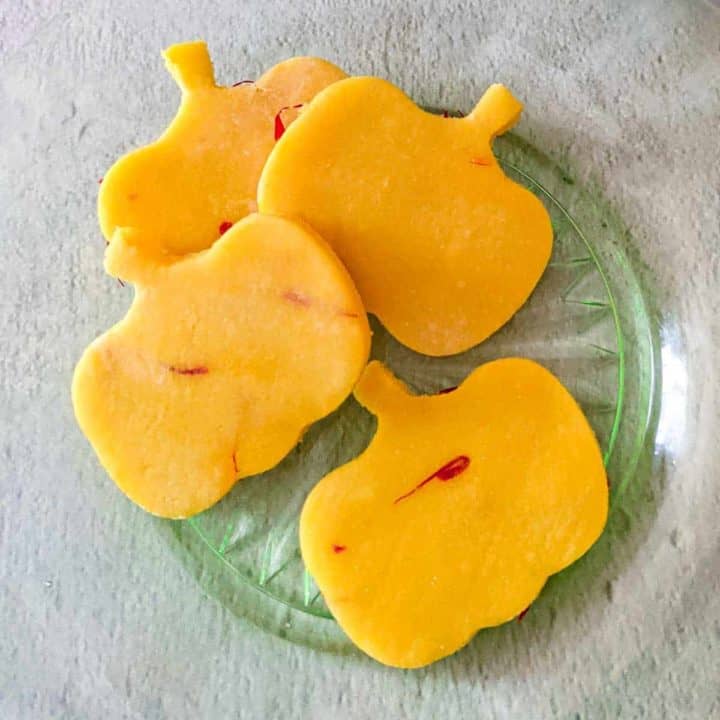 Overhead photo of four pumpkin-shaped pieces of rosewater-saffron marzipan on a green glass plate