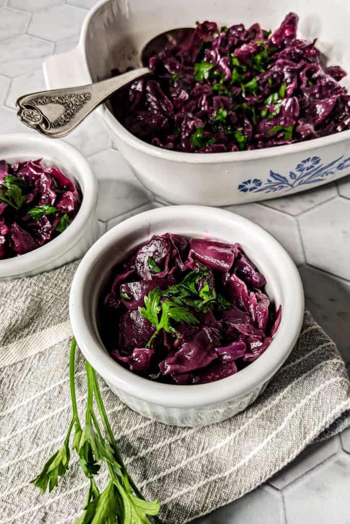 Side-view photo of a serving dish and two individual portions of braised red cabbage with caraway seeds