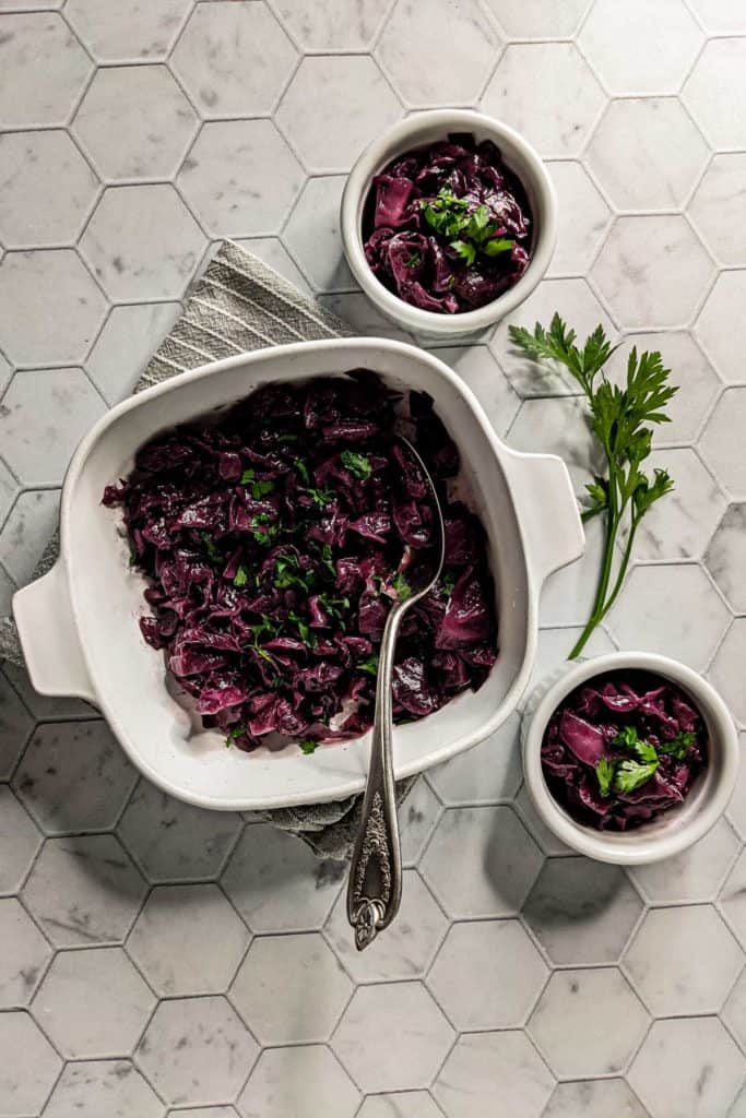 Overhead photo of a serving dish and two individual portions of braised red cabbage with caraway seeds