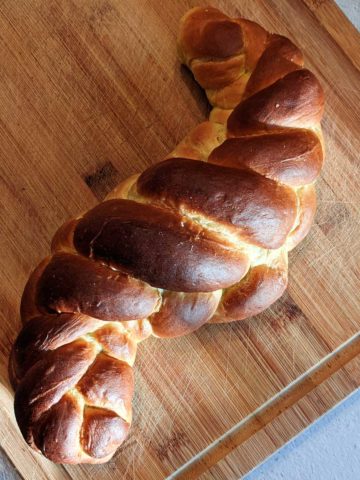 overhead photo of a braided loaf of challah on a wooden cutting board
