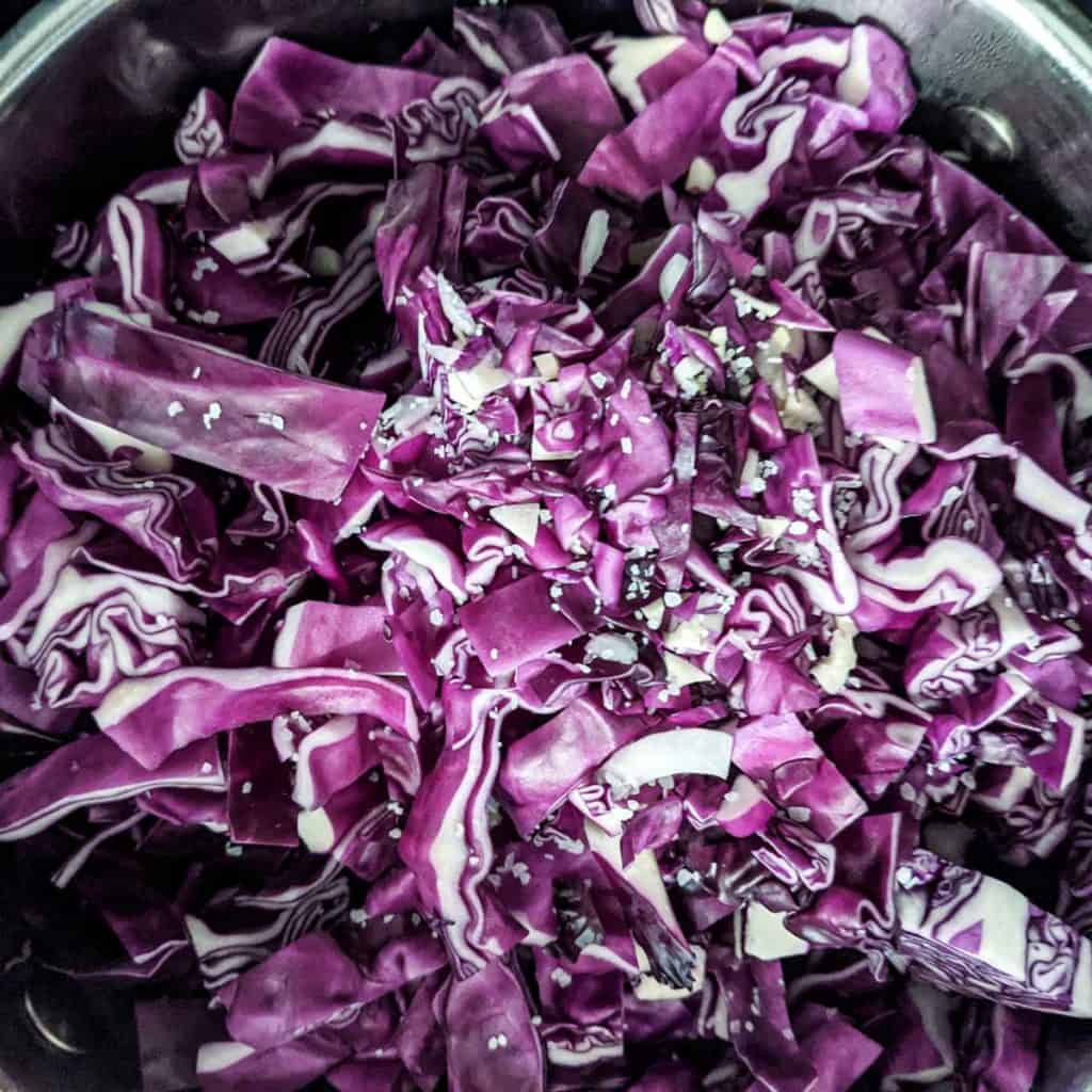 overhead photo of raw chopped red cabbage being added to large braising pan