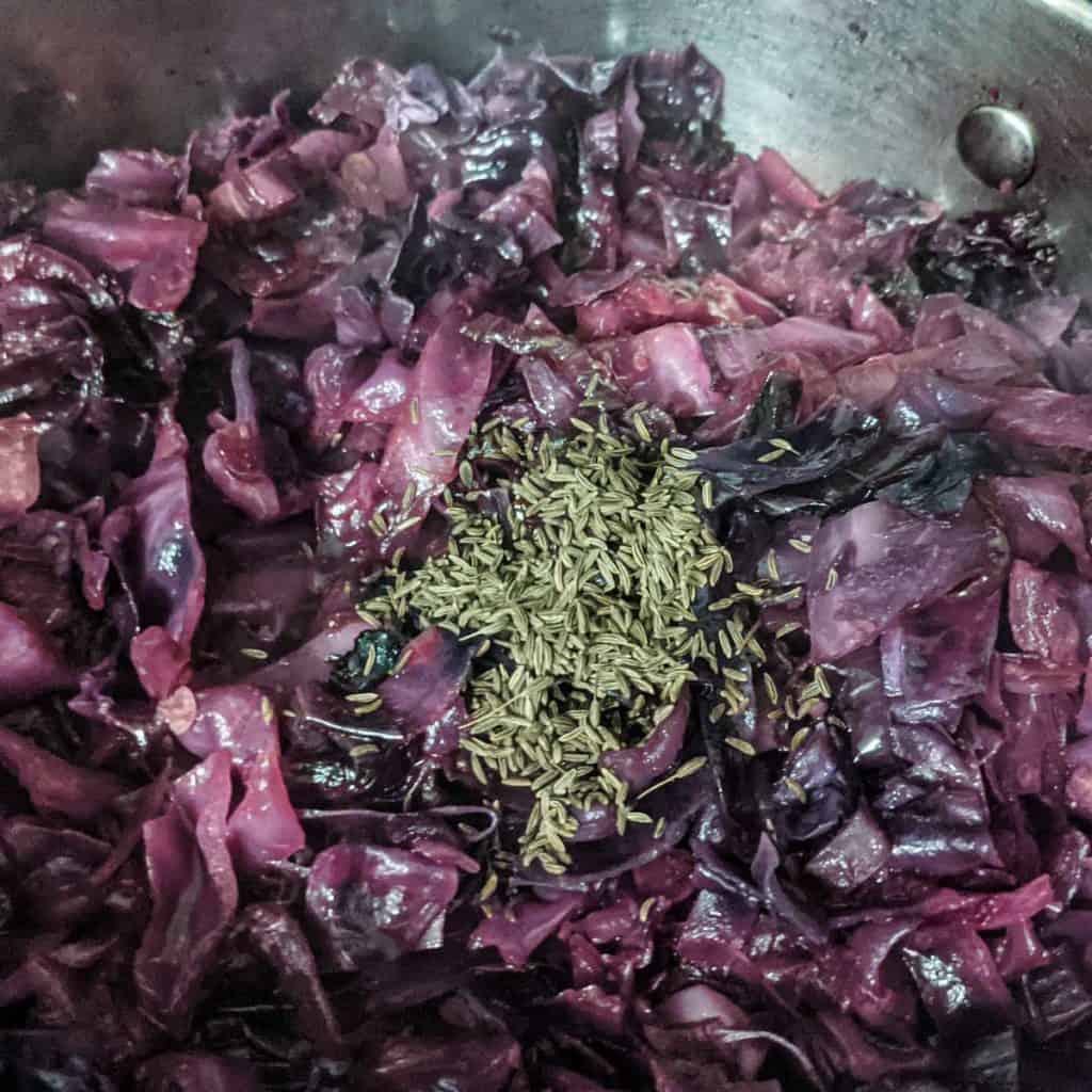 Overhead photo of vinegar and caraway seeds being added to braised red cabbage