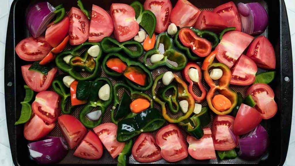Overhead photo of a baking sheet of fresh vegetables to be roasted for vegan chili