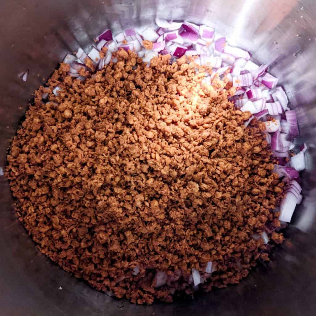 Overhead photo of a large pot with chopped onions and vegan beef crumbles
