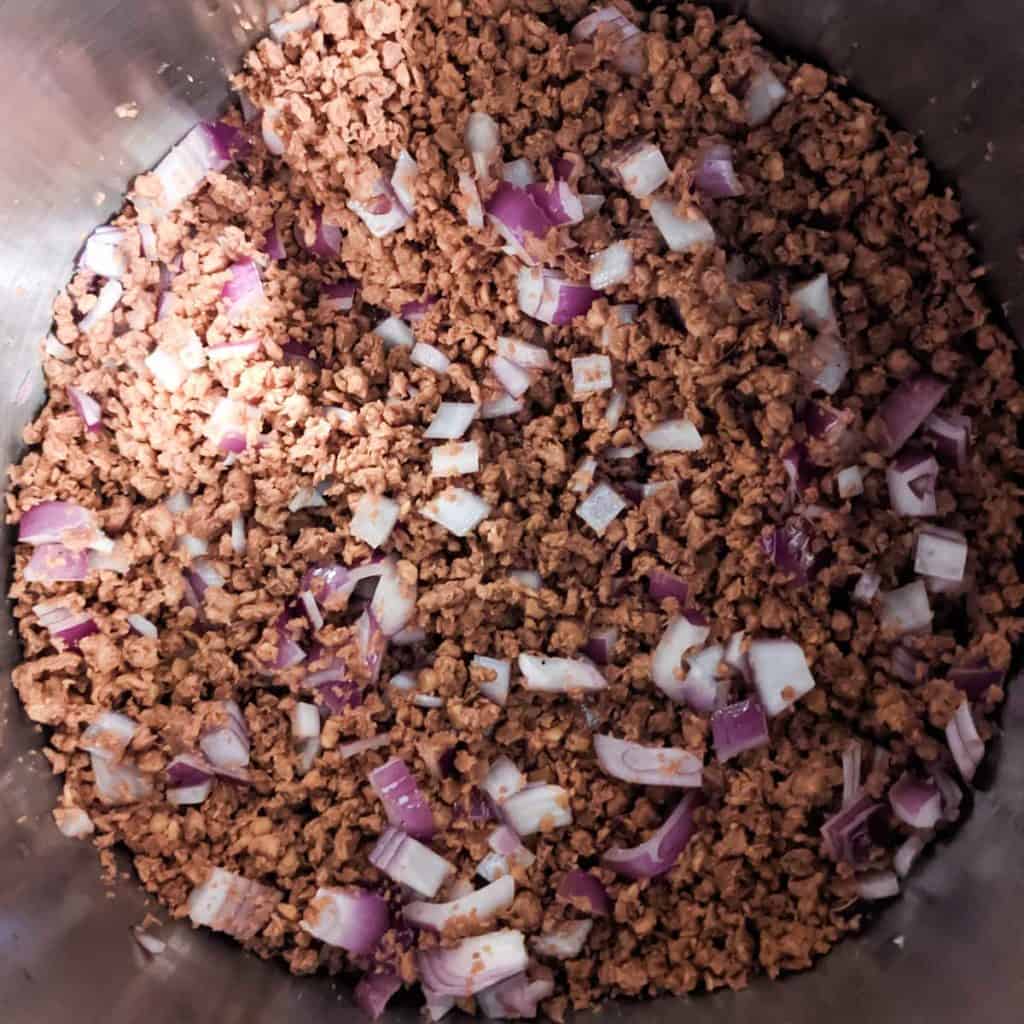 Overhead photo of a large pot with translucent chopped onions and browned vegan beef crumbles