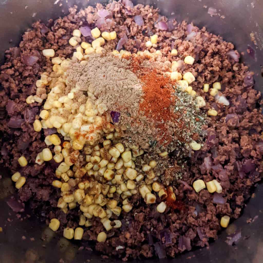 Photo of adding the corn and spices to the vegan beef and onion