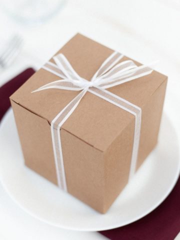 Photo of a box wrapped with a bow, placed on a white plate with a burgundy napkin