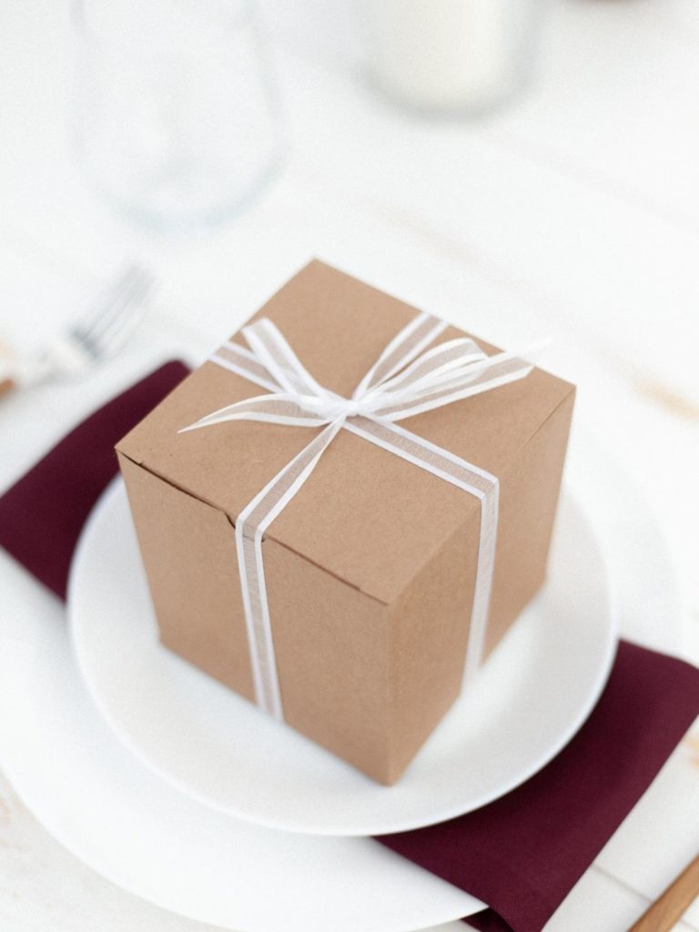 Vegan gift ideas: photo of a box wrapped with a bow, placed on a white plate with a burgundy napkin