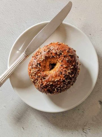 Overhead photo of a bagel on a white plate with a knife