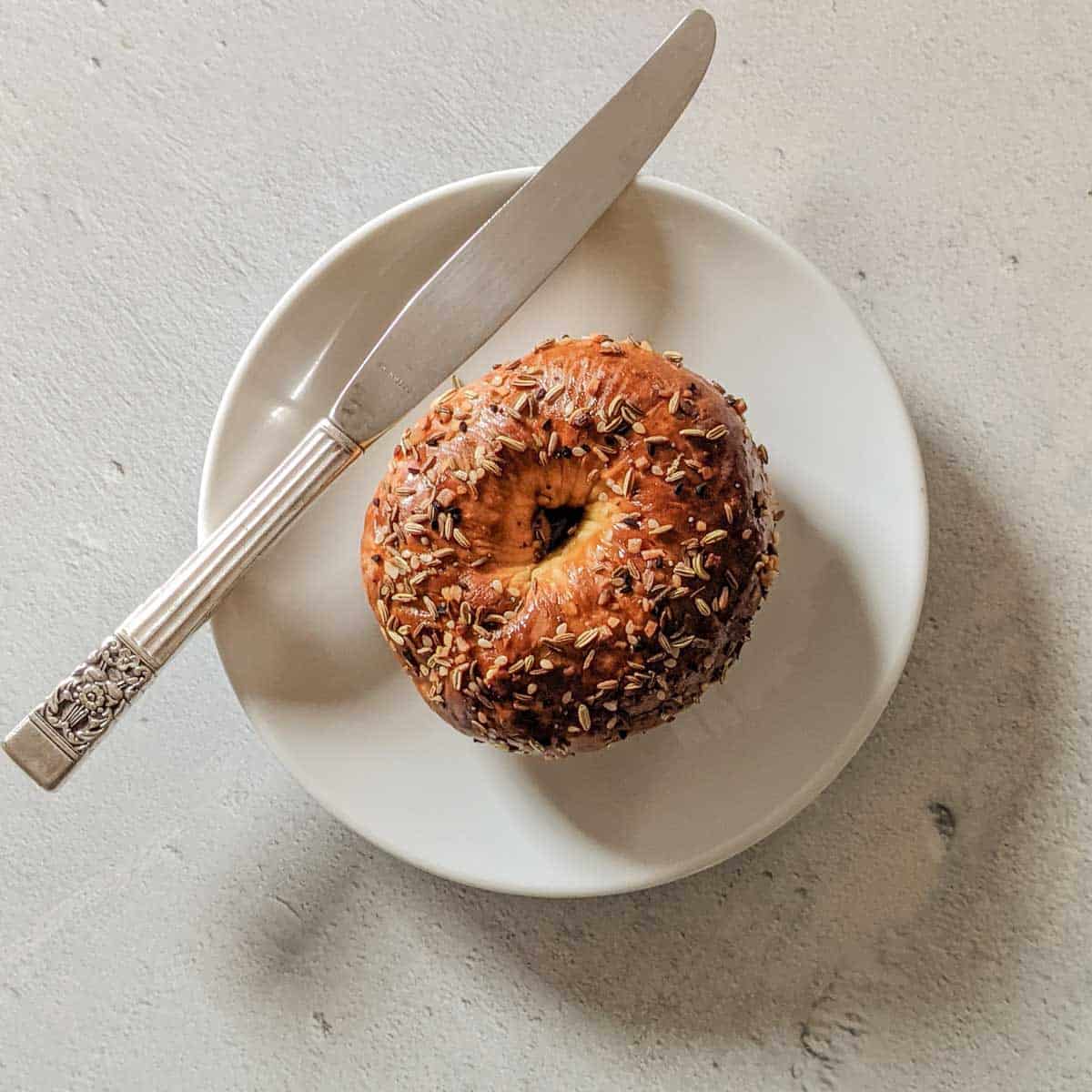 Overhead photo of a bagel on a white plate with a knife