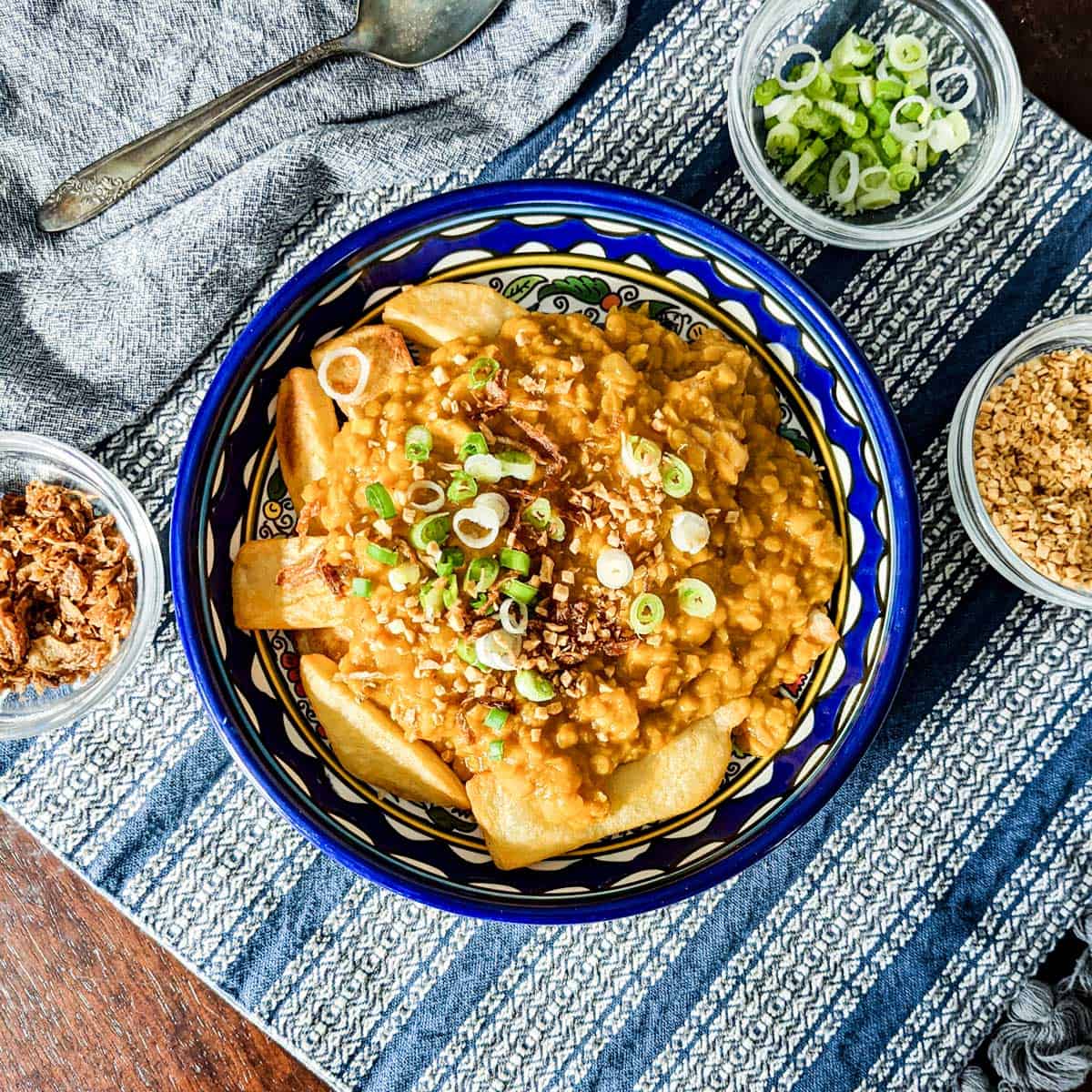 Overhead photo of a bowl of red lentils served over potatoes with assorted garnishes