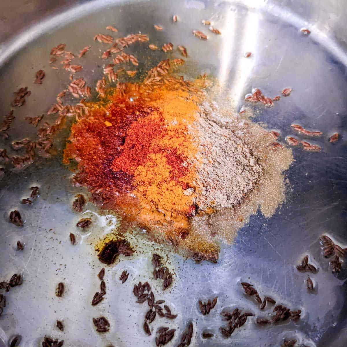 photo of a stainless steel pan with oil, cumin seeds, turmeric, coriander, and paprika