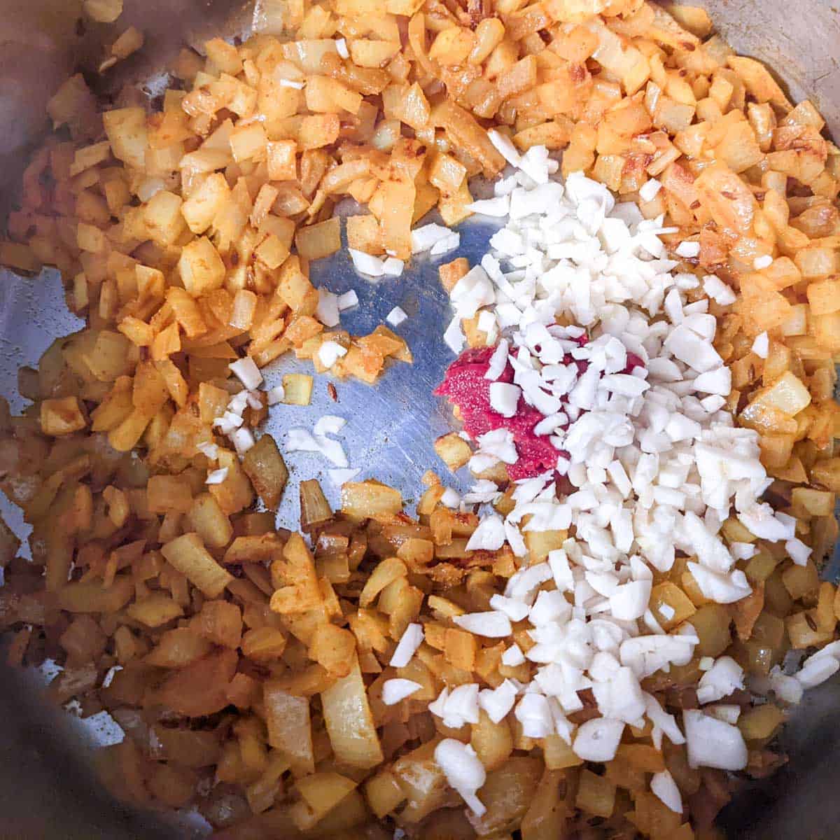 Overhead photo of a pan with tomato paste,garlic, and chopped onions and spices