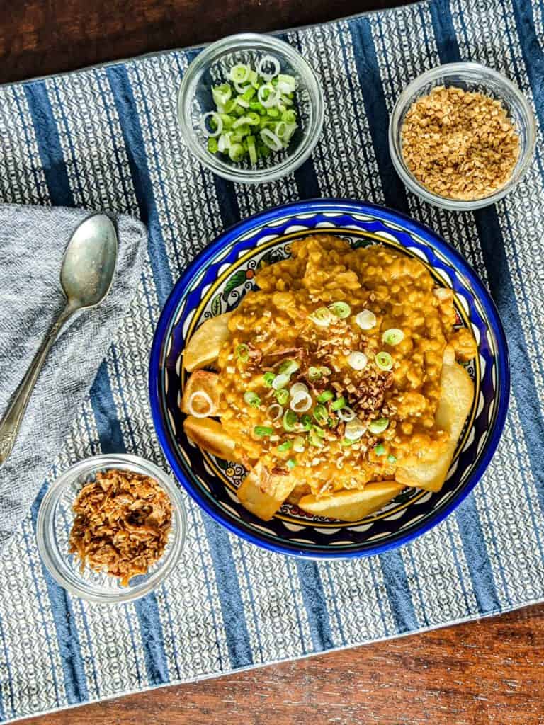 Overhead photo of a bowl of spiced lentils over potatoes with smaller bowls of toppings on a striped placemat with a spoon and napkin